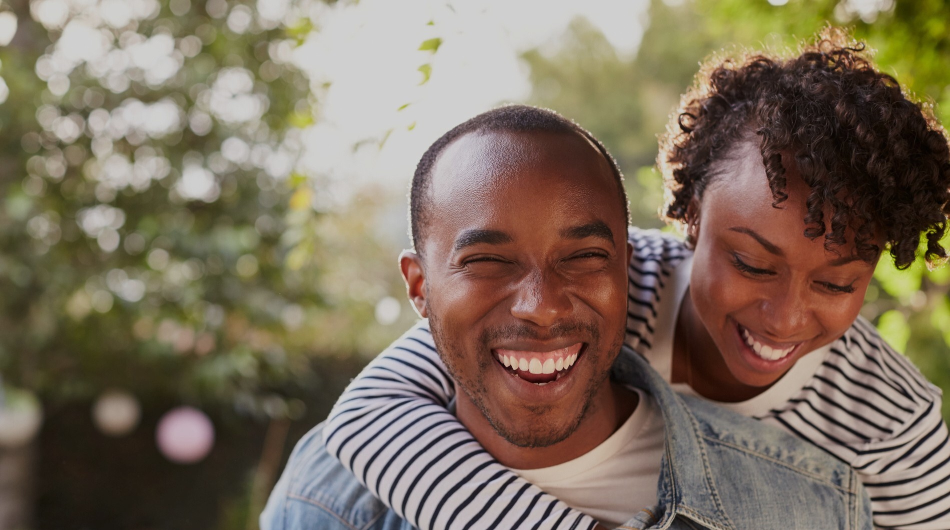 Laughing young black couple piggyback in garden, to camera People smiling after minor teeth straightening in Crestview Hills KY